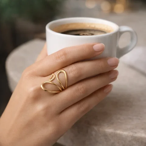 Anillo nube dorado de acero inoxidable ajustable puesto en la mano mientras sostiene una taza de café.