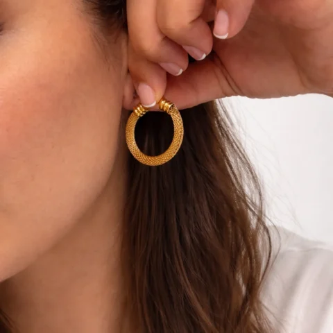 aros dorados trenzados puestos en oreja mujer