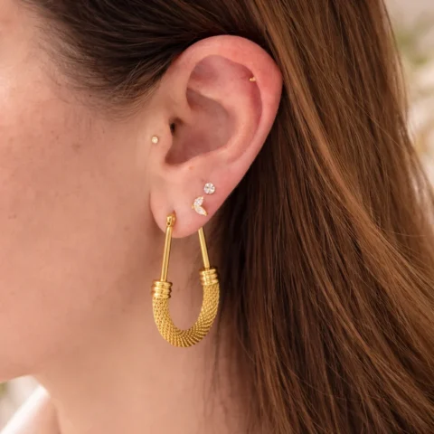 Aros dorados elegantes con textura trenzada puestos en oreja